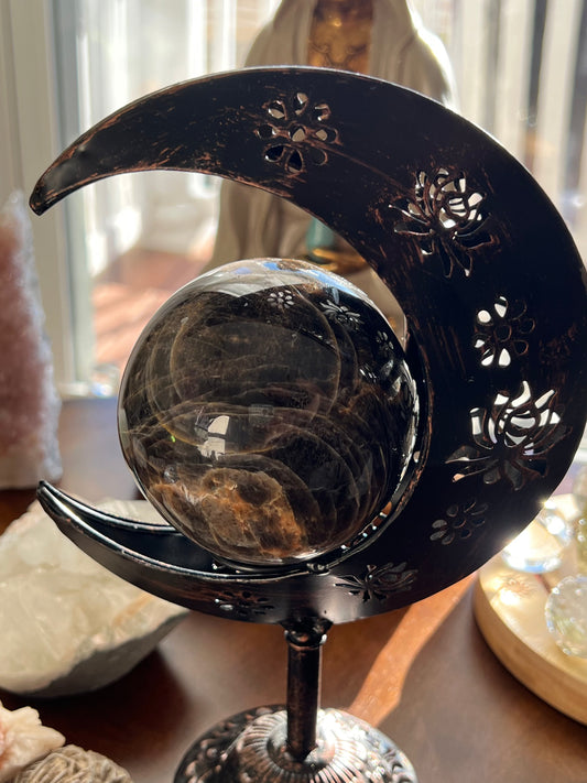 Smoky crystal ball held by decorative metal crescent moon stand.