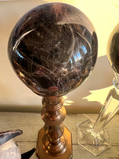 A dark brown crystal ball rests on a gold metal stand.