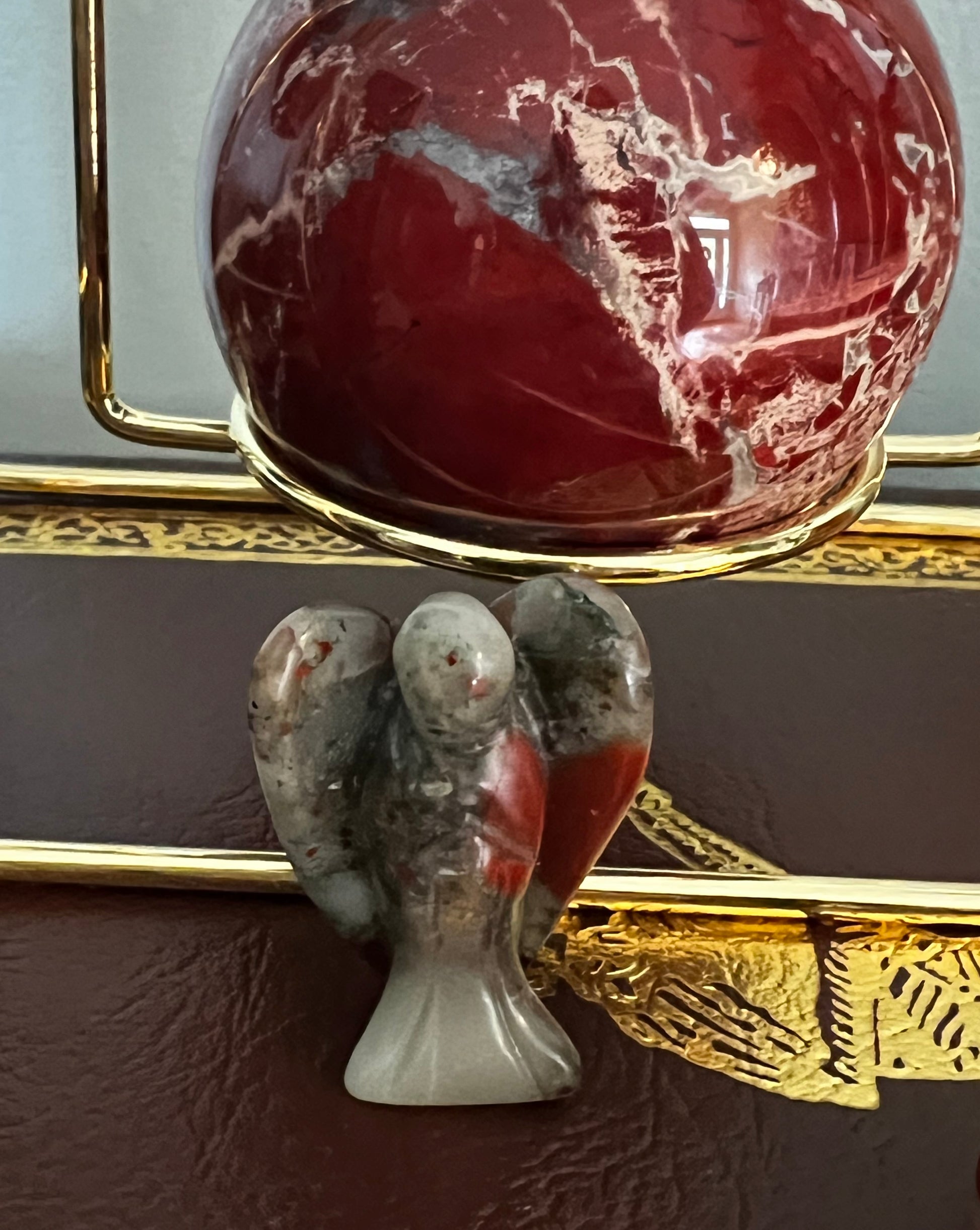 Close-up of a small stone angel figurine and a red, mottled sphere in a gold stand.