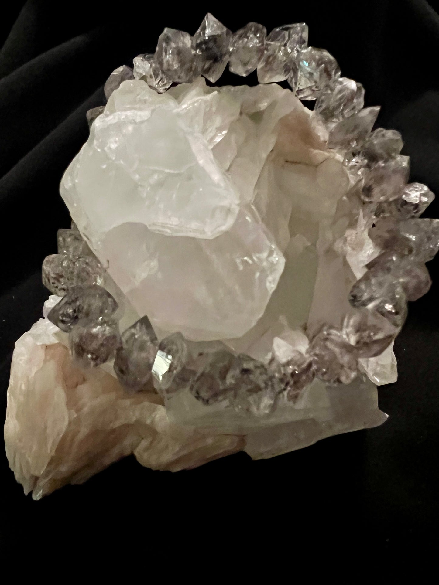 A crystal bracelet rests atop a larger mineral formation against a black background.