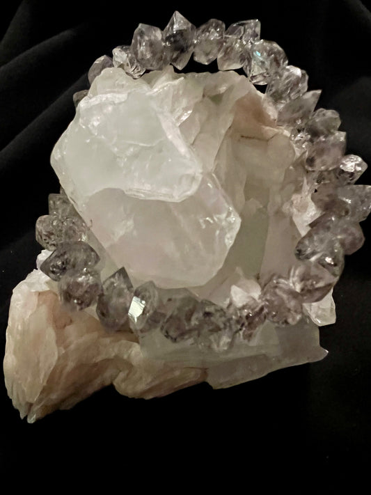 A crystal bracelet rests atop a larger mineral formation against a black background.