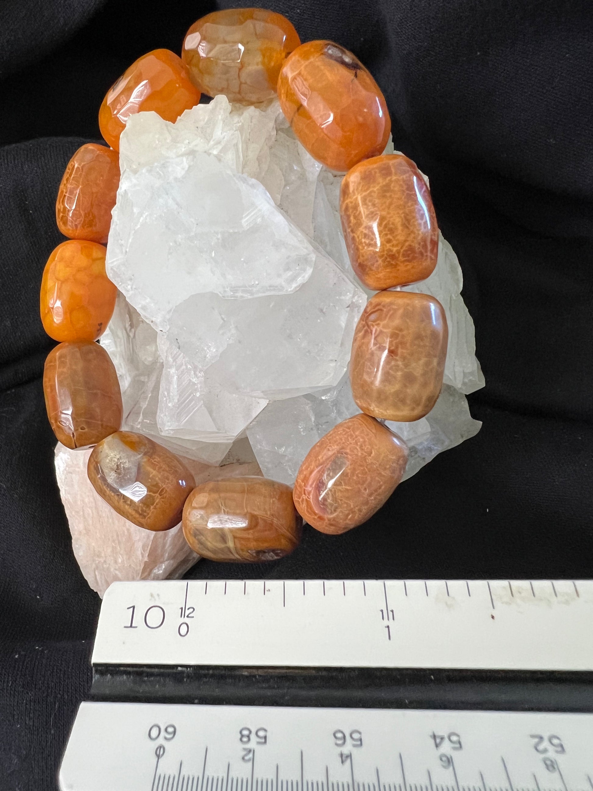 Close-up of an orange stone bracelet on a white crystal, with a white ruler in the foreground on a black background.