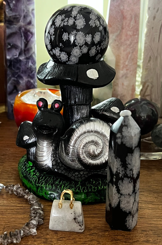 A collection of whimsical decorations including a snowflake obsidian sphere atop a mushroom, a snail figure, a small purse, and a crystal tower.