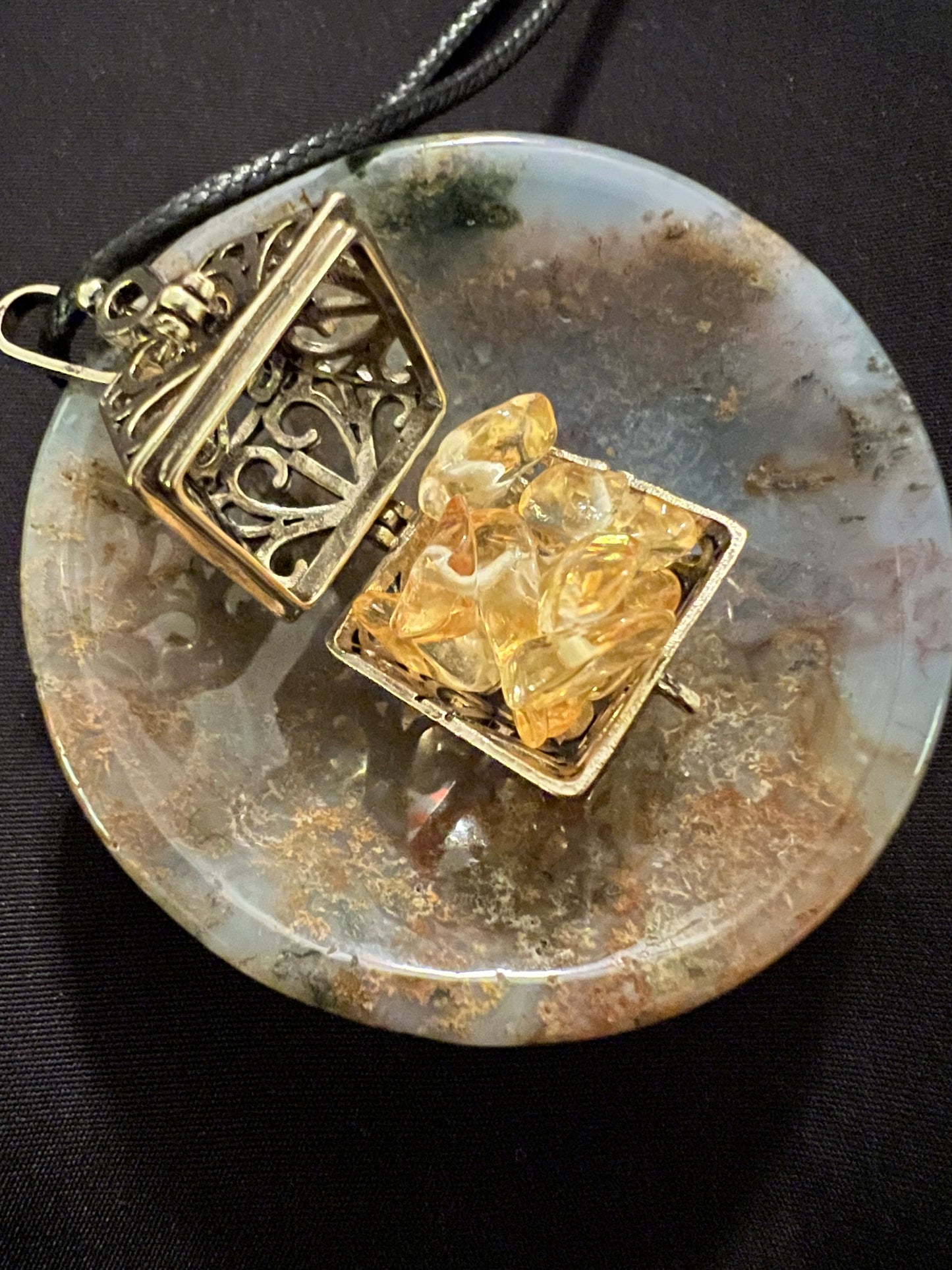 Open gold locket with citrine crystals on round agate pendant with black cord.
