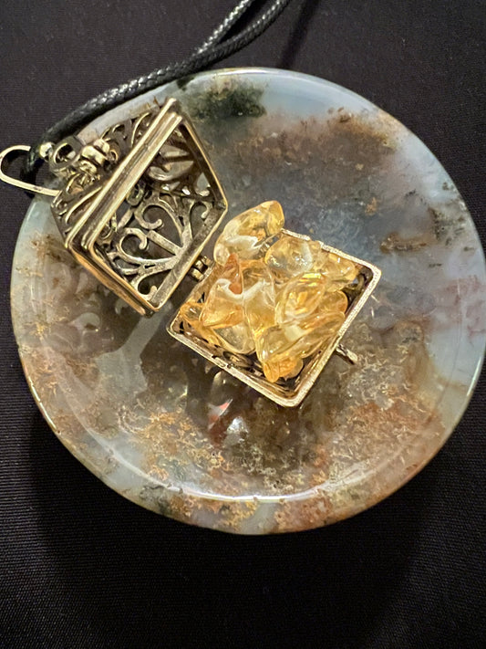 Open gold locket with citrine crystals on round agate pendant with black cord.
