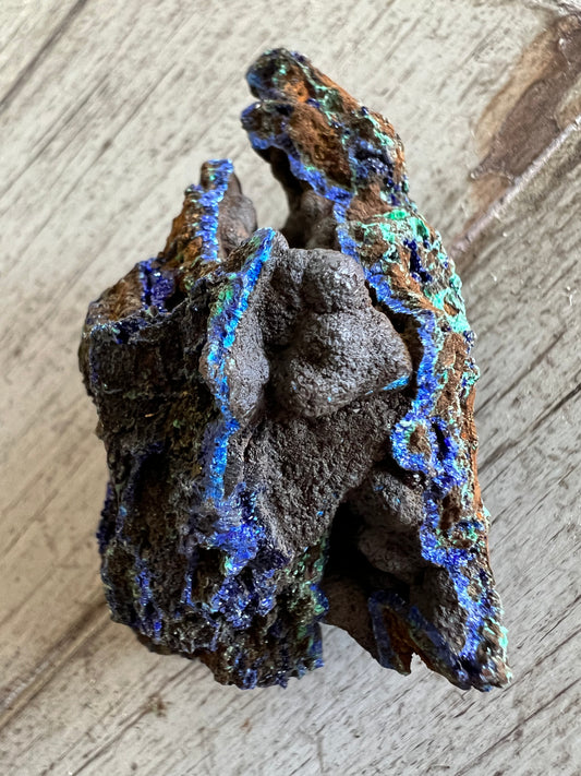 Chunk of dark rock with bright blue and green accents, resting on a wooden surface.