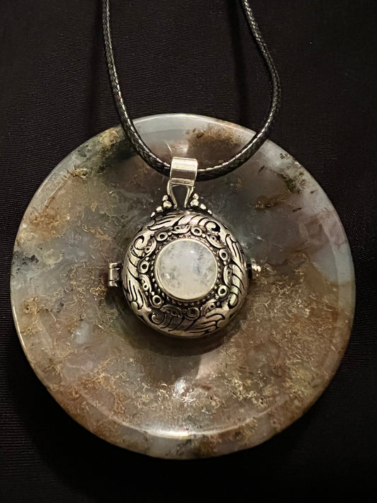 Silver locket necklace with moonstone pendant on polished moss agate.