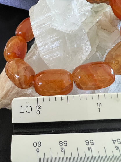 Close-up of an orange carnelian gemstone bracelet against a white crystal, measured with a ruler.
