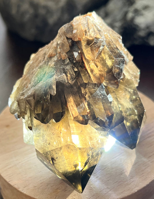 Close-up of a cluster of brown and clear crystals on a wooden base, backlit for display.