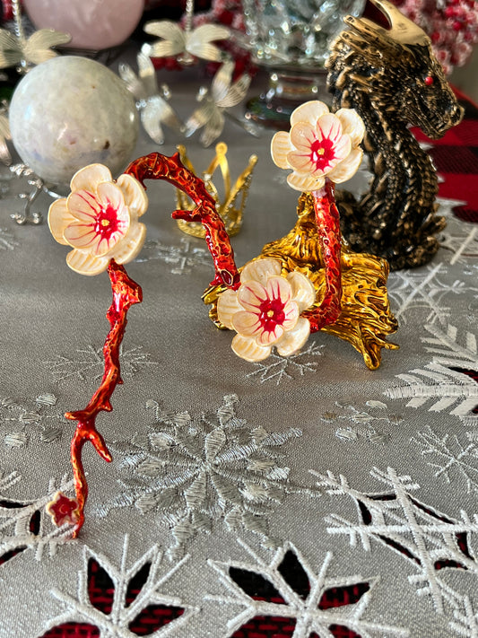 Ornate jewelry display with red branches and white-petaled flowers, against a backdrop of silver snowflake fabric and golden figurines.

