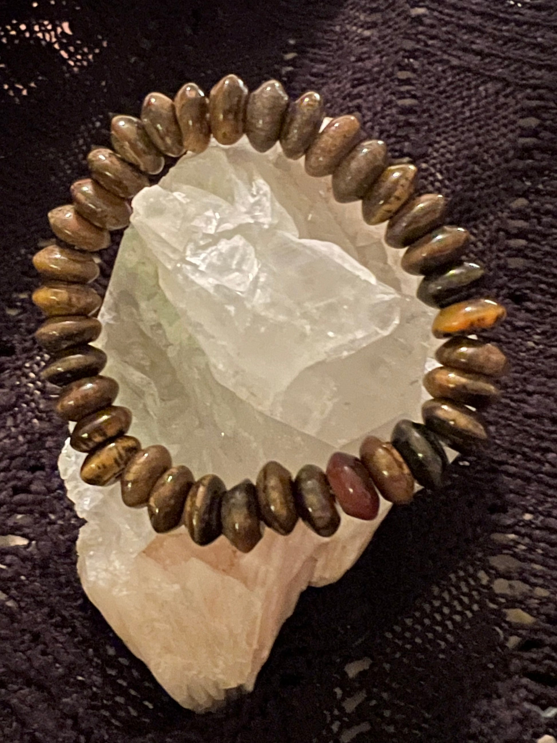 A bracelet of rounded brown stones rests on a white quartz crystal against a dark, textured background.
