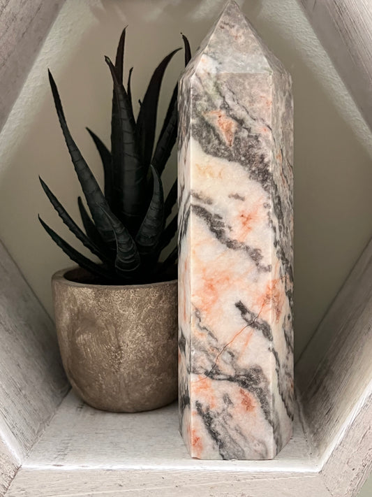 A faux aloe plant in a golden pot next to a marble pillar inside a hexagonal shelf.