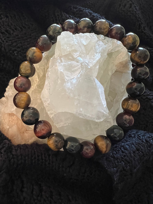 Bracelet made of brown, red, and black stone beads, wrapped around a clear crystal on a dark knit background.