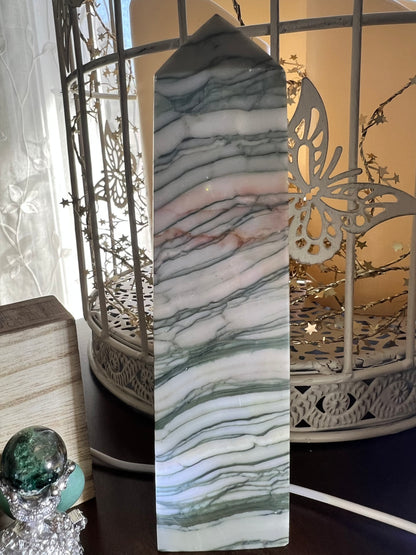 A green and white striped gemstone tower stands in front of a white decorative bird cage and fairy lights.