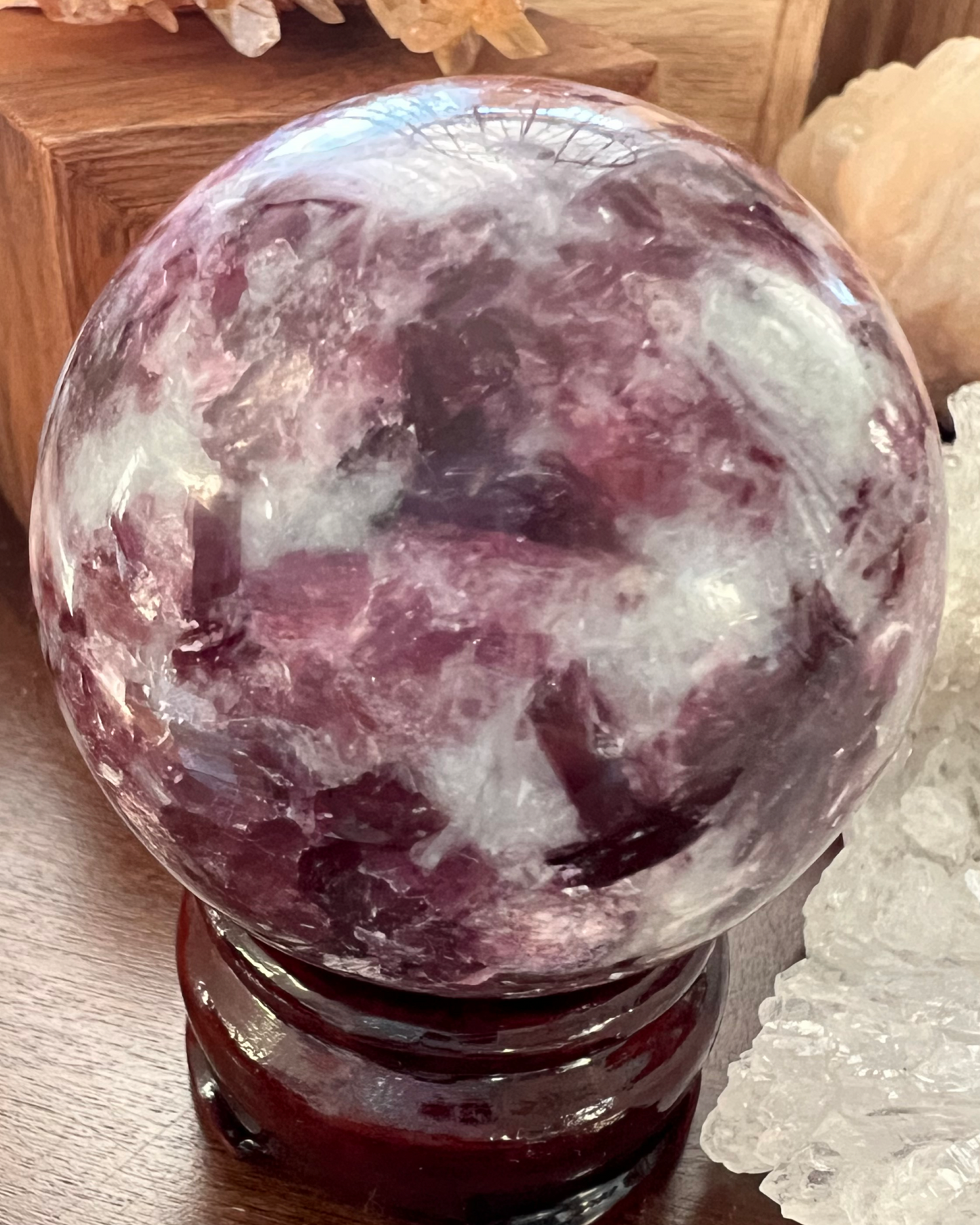 A round, polished lepidolite sphere on a dark brown wooden stand.