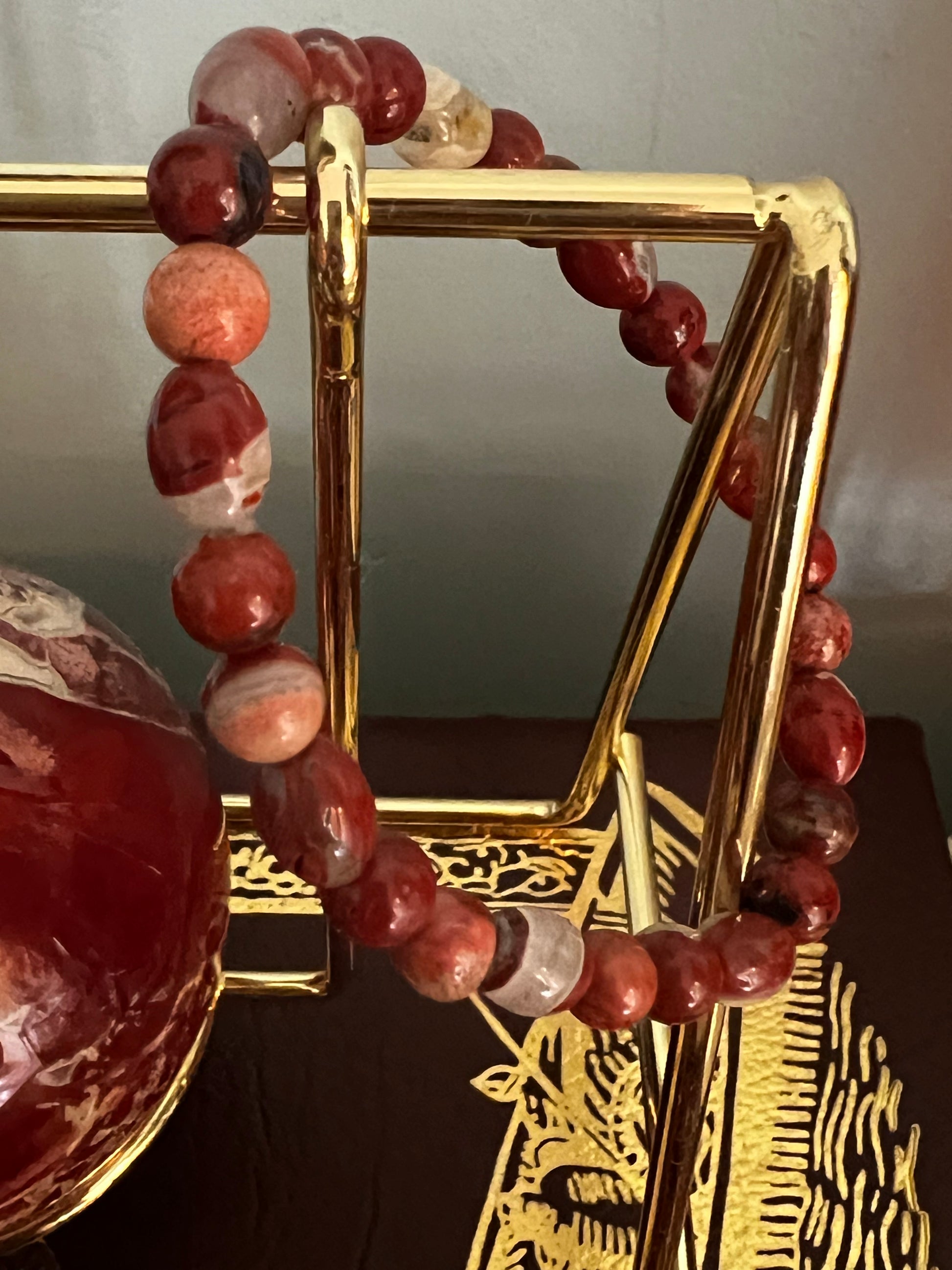 Red and white beaded bracelet draped on a gold stand.