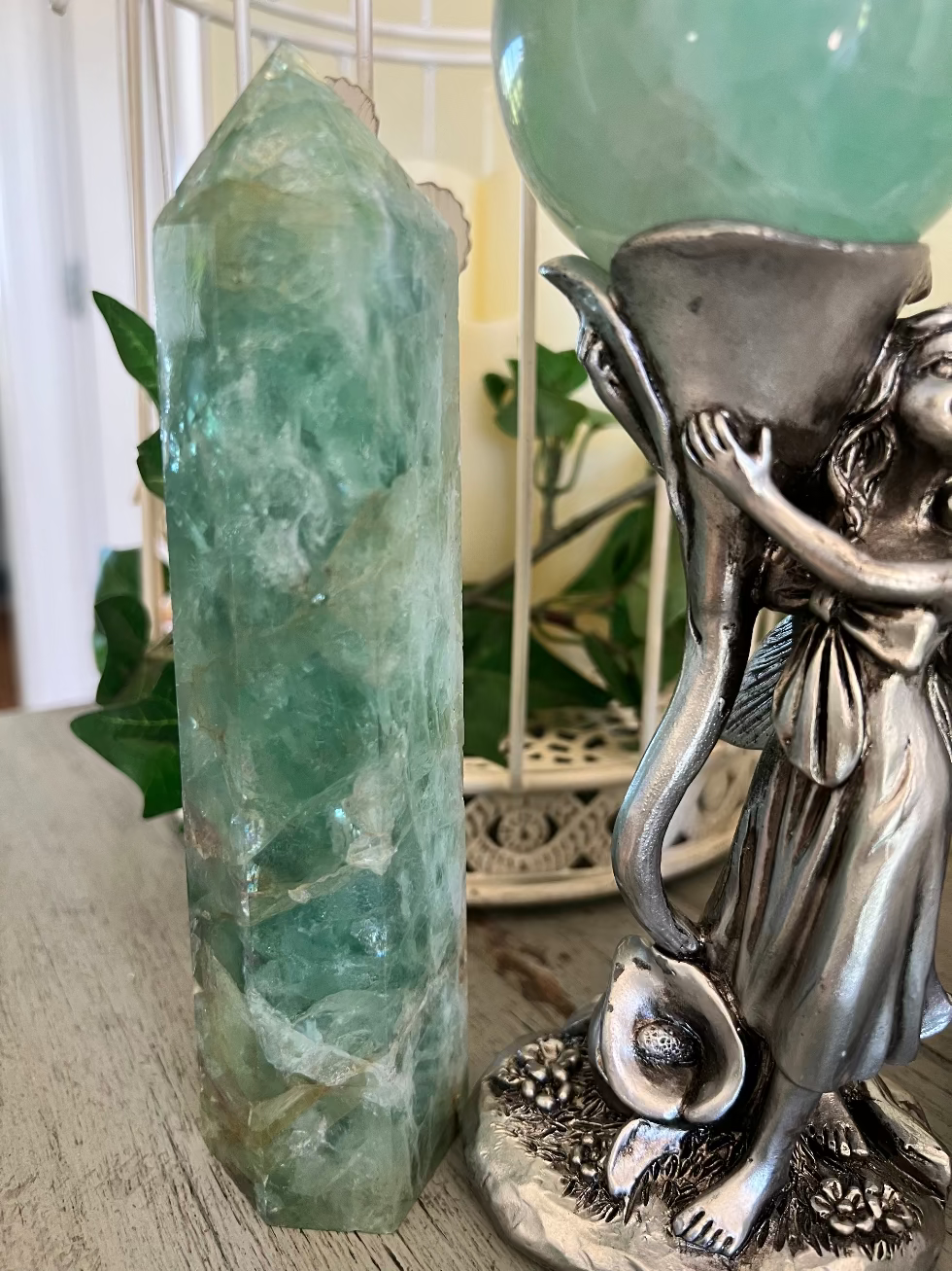 A green crystal point stands next to a silver fairy statue holding a green crystal ball.