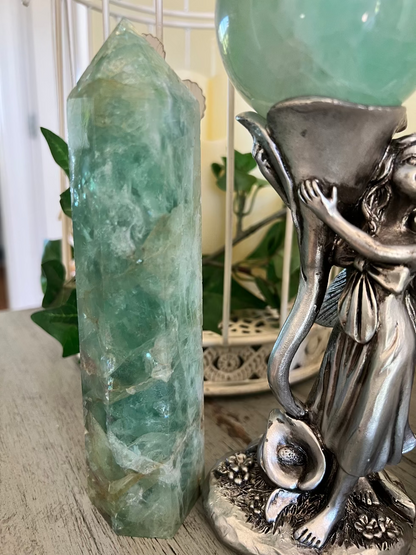 A green crystal point stands next to a silver fairy statue holding a green crystal ball.