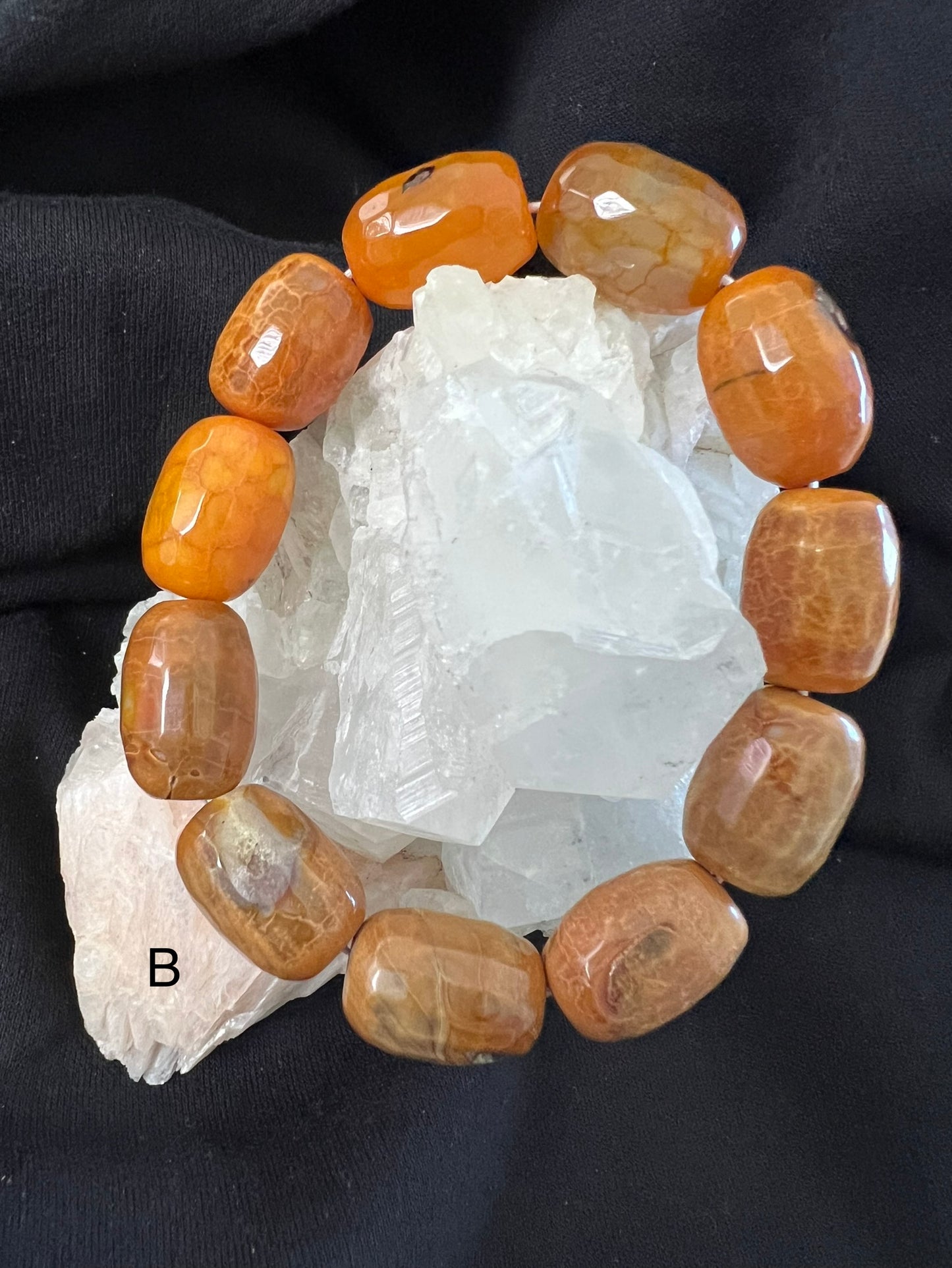 Close-up of an orange gemstone bracelet on clear quartz, resting on black fabric.