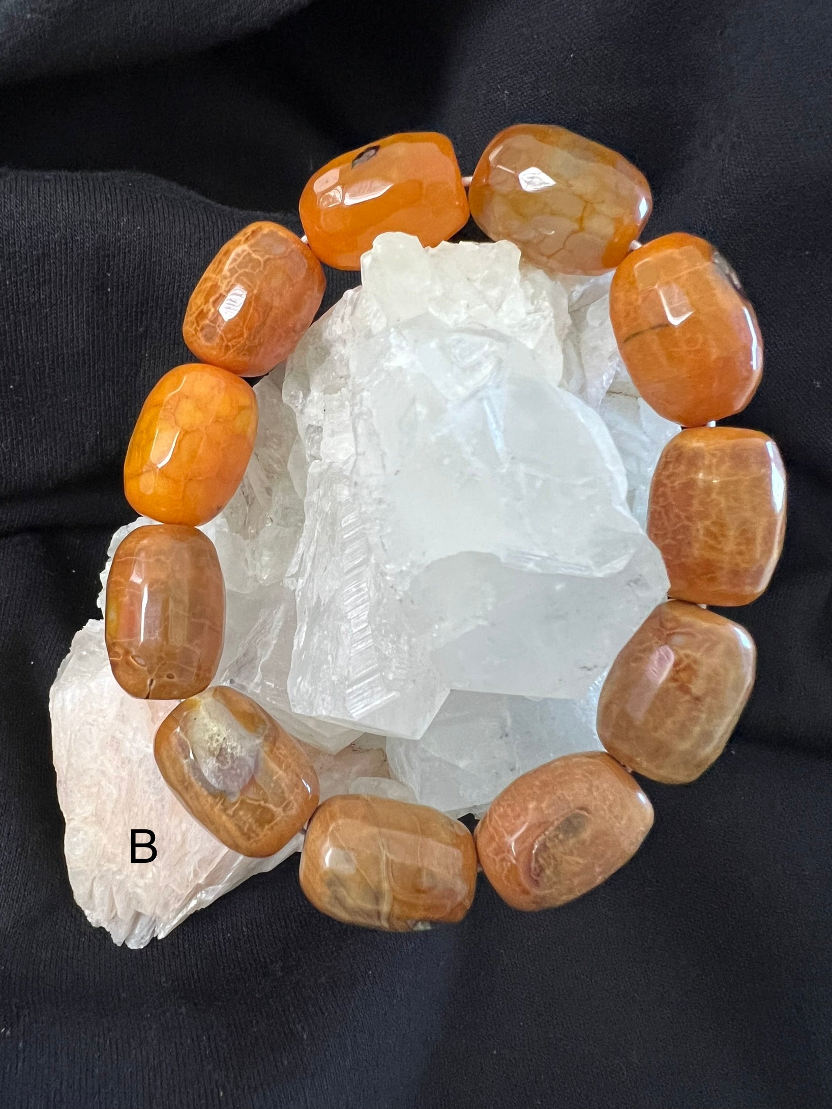 Close-up of an orange gemstone bracelet on clear quartz, resting on black fabric.