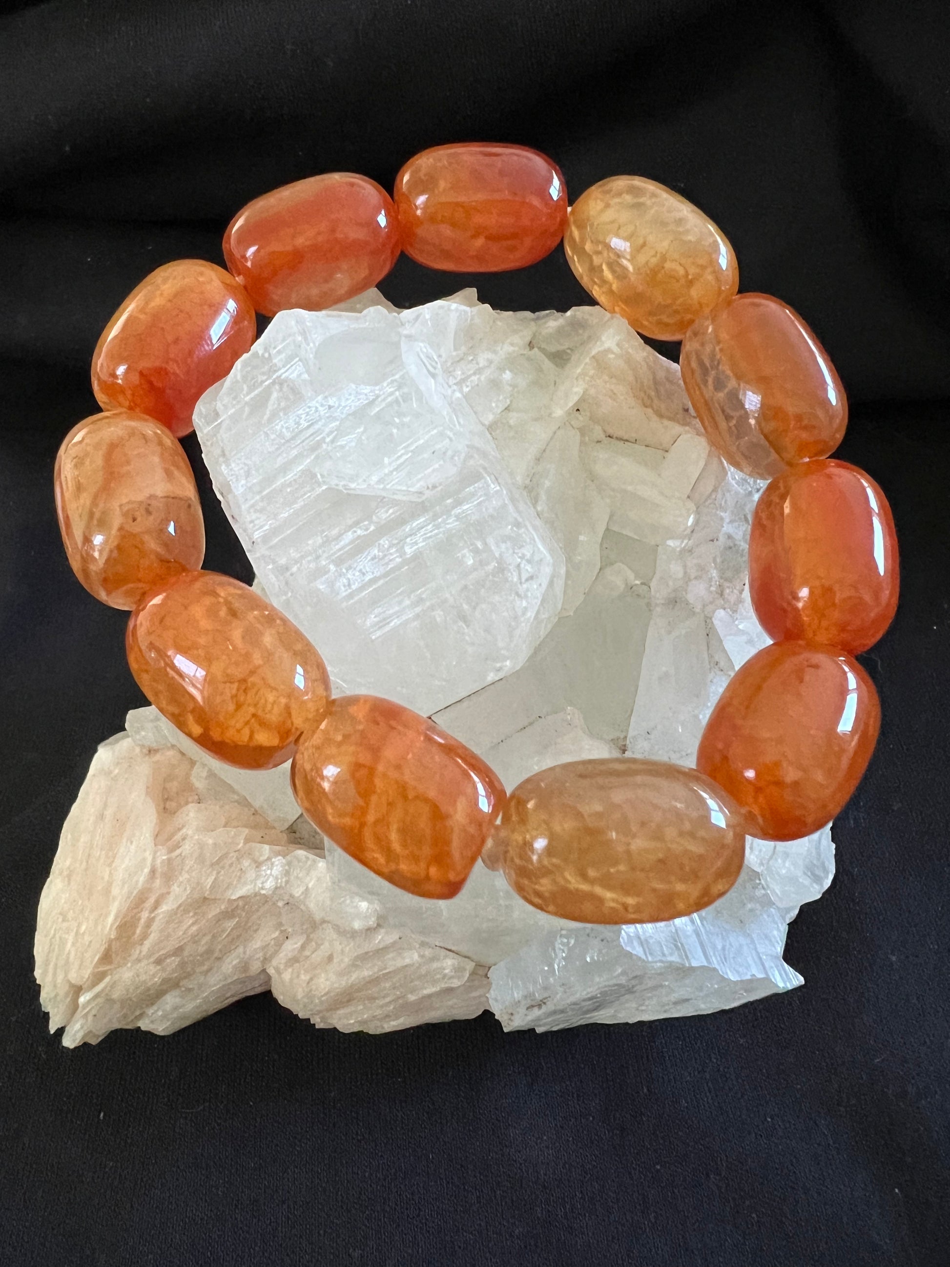 Orange bead bracelet on a cluster of clear crystals, against a black background.
