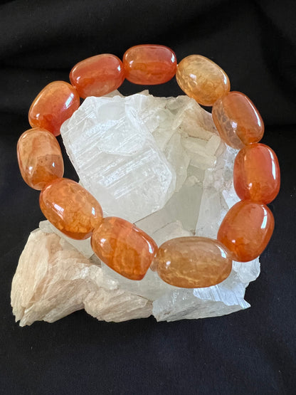 Orange bead bracelet on a cluster of clear crystals, against a black background.
