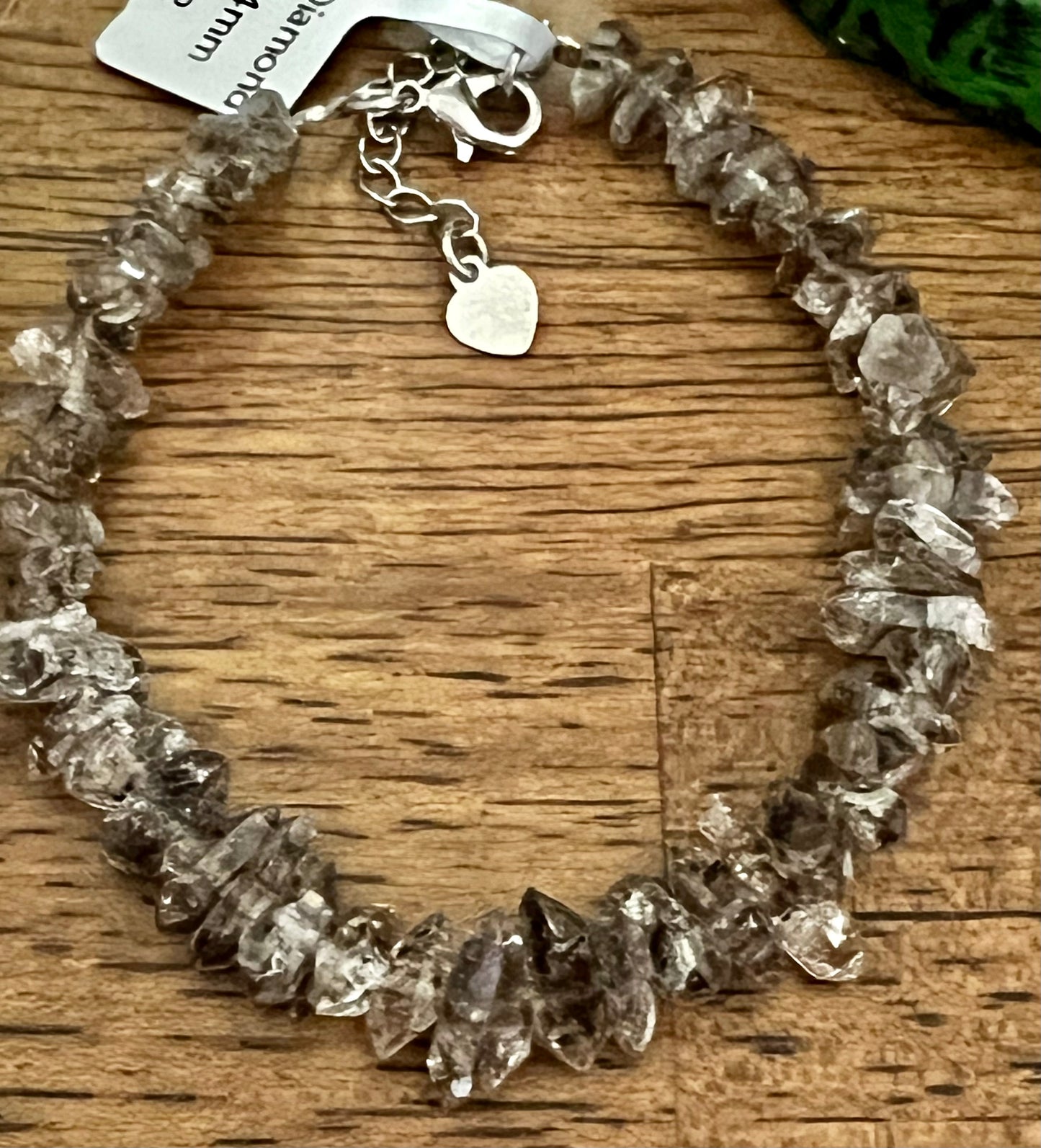 Close-up of a smoky quartz bracelet with a silver clasp and heart charm, set on a wooden surface.