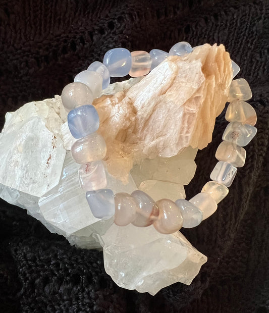 A pale blue and pink gemstone bracelet is wrapped around a light-colored crystal formation, set against a black background.