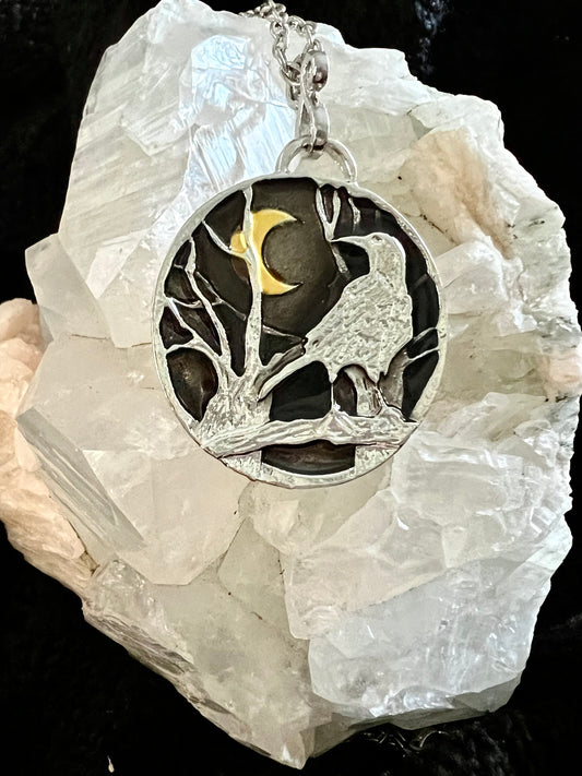 Silver pendant necklace with a raven and crescent moon design, resting on a crystal.