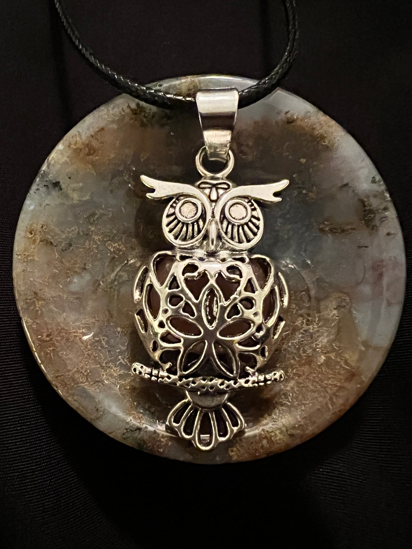 Owl pendant on stone disk with black cord.