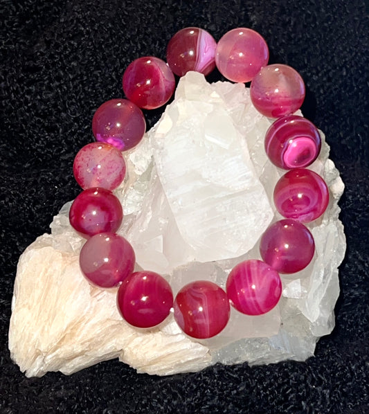 Bright Pink Agate Bead Bracelet displayed on a white rock. black background 